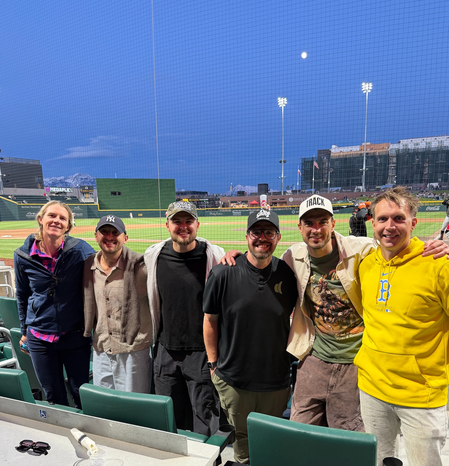 Friends in stadium seats at a ballpark with snow-capped mountains behind