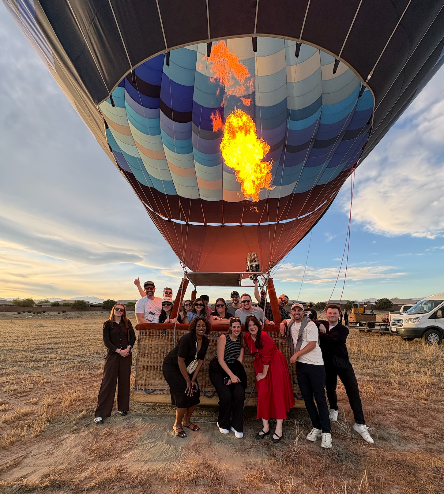 Large group posing under a hot air balloon firing its flames at golden hour