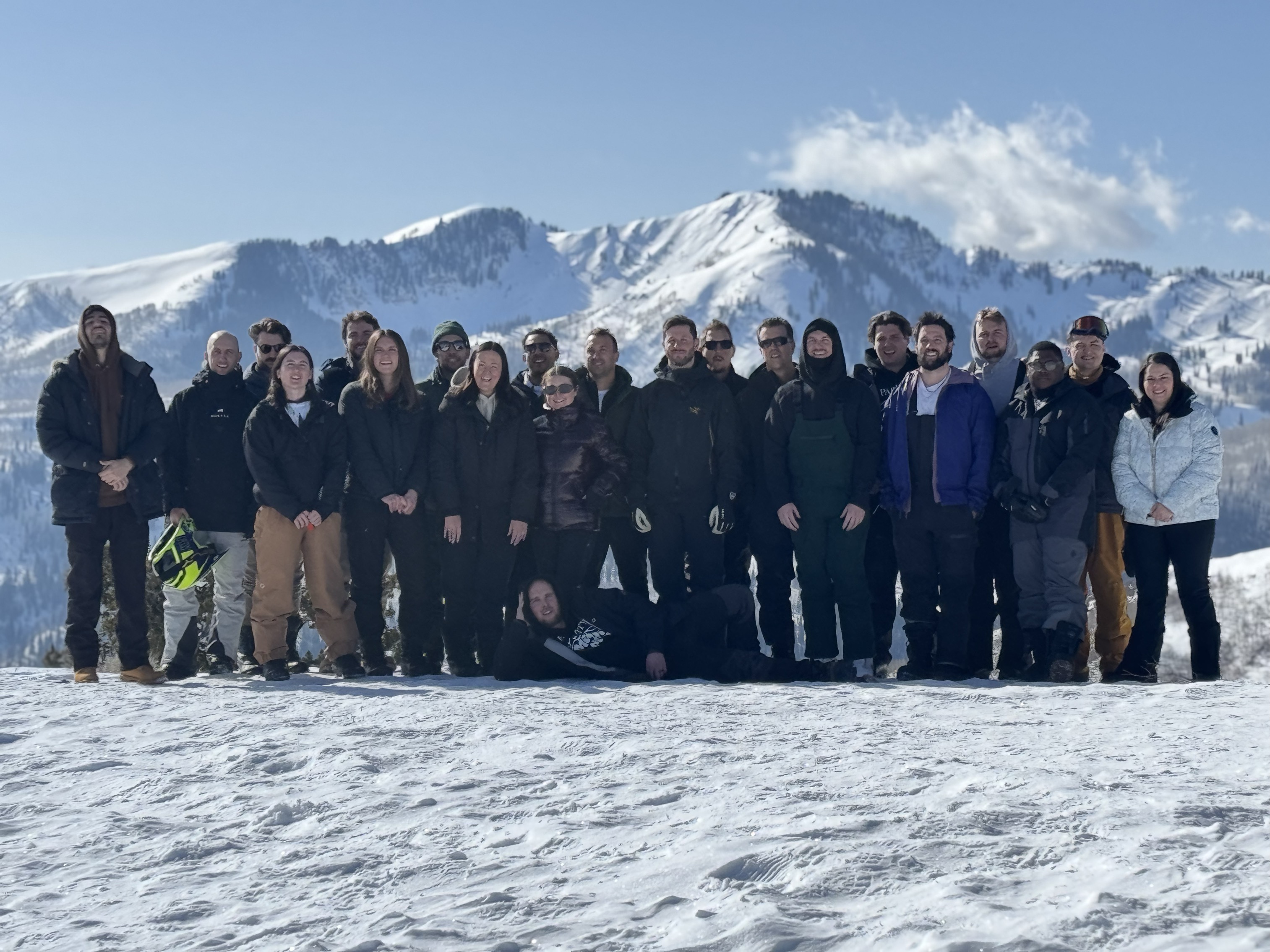 Large group on a snowy mountain slope with peaks in the background