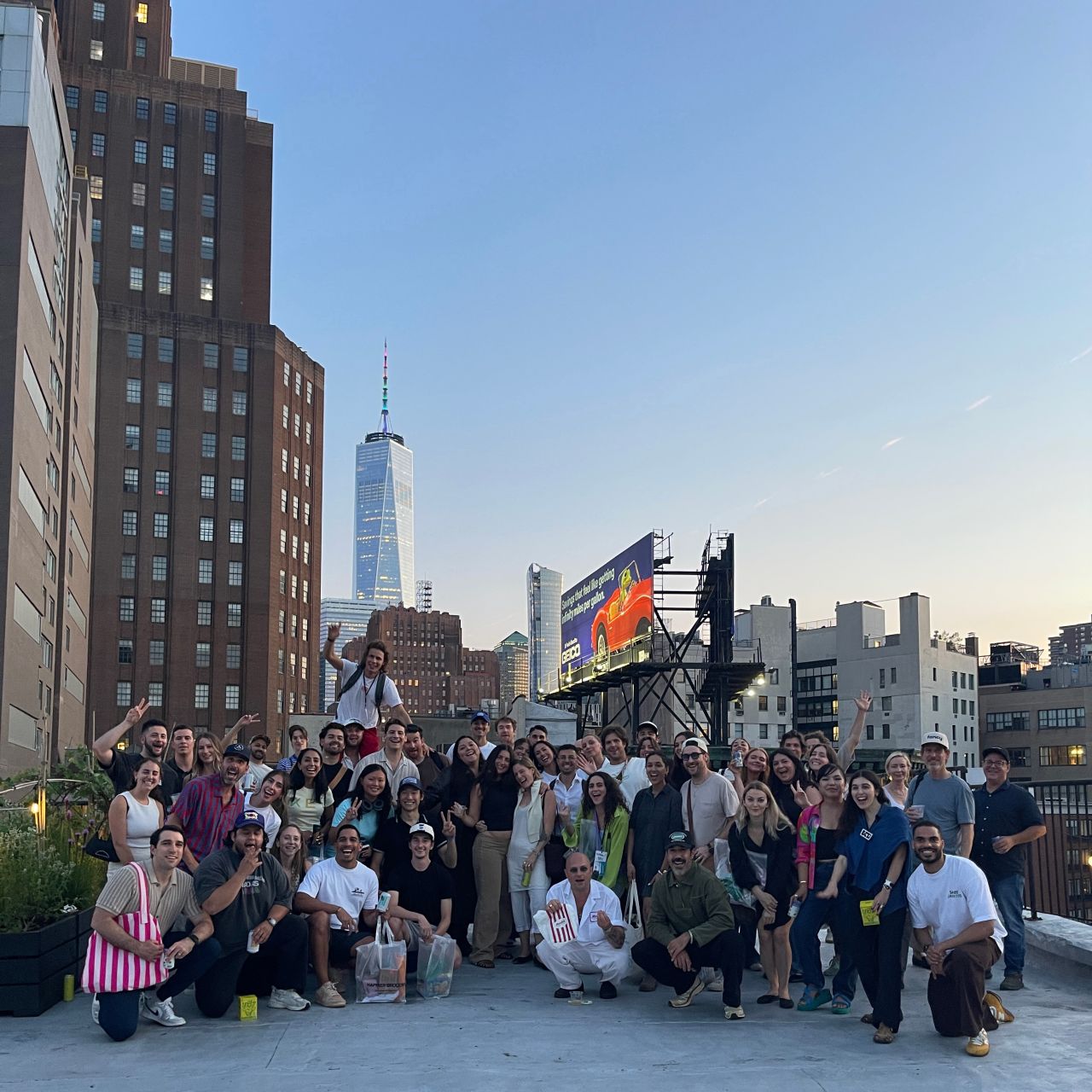 Huge community group photo on a Manhattan rooftop at dusk with One World Trade behind