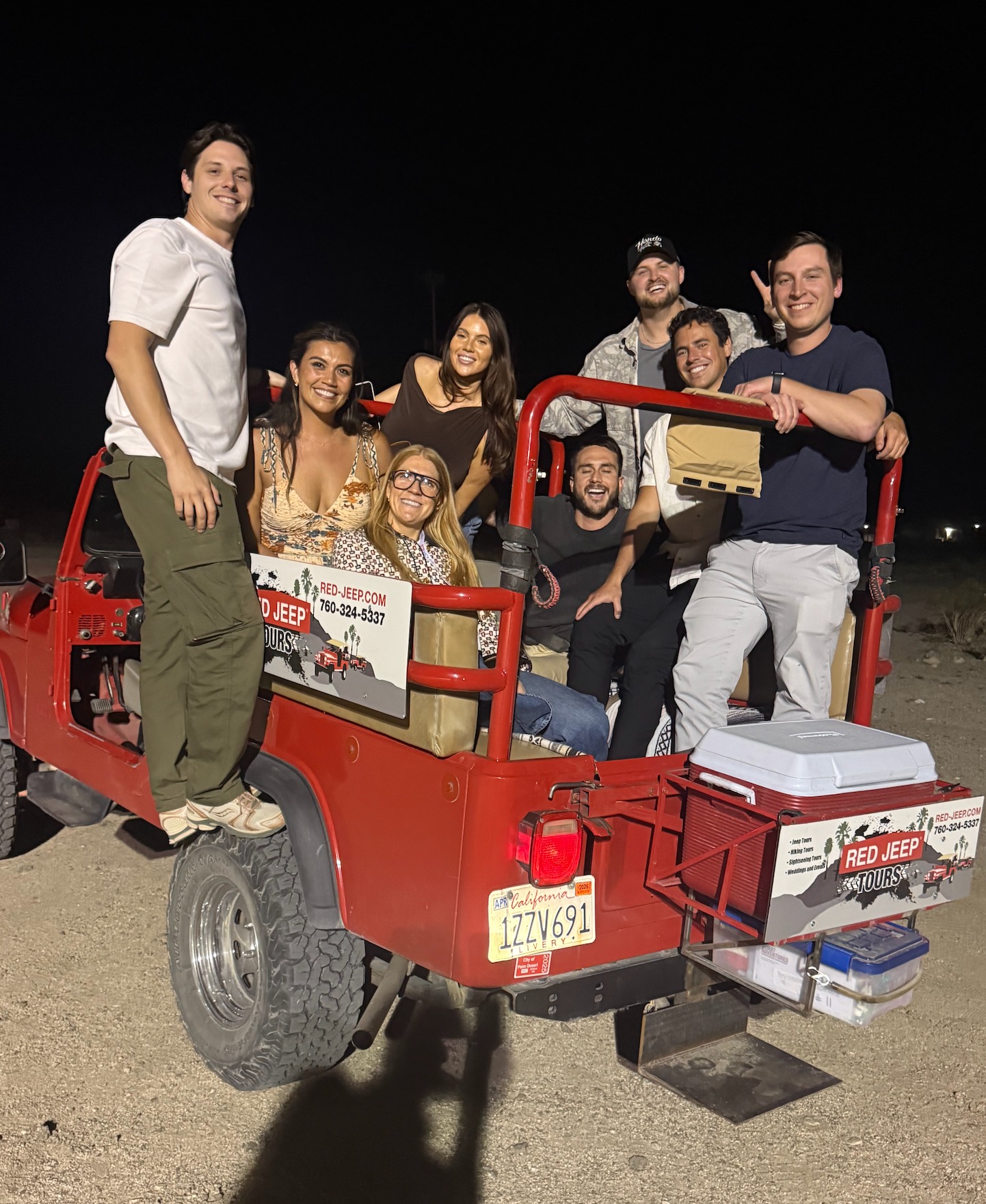 Group piled onto a red Jeep at night in the desert